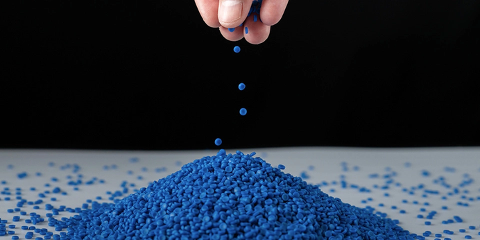 A hand dropping blue plastic pellets onto a pile